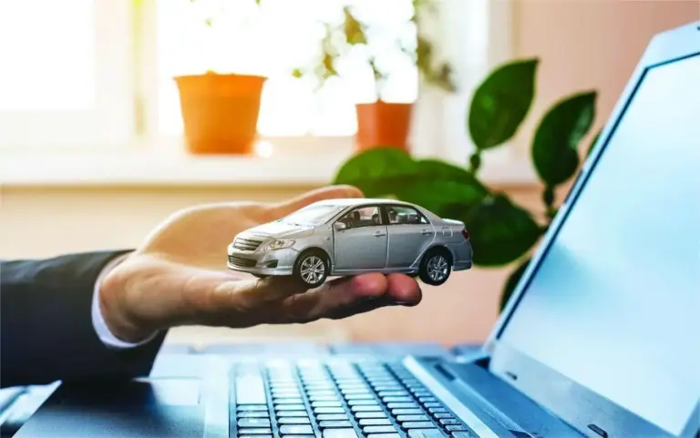 a man hold toy car on his hand front of laptop